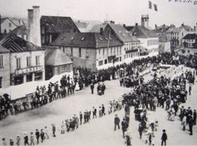 La place du Général-de-Gaulle animée par une foule, photographie ancienne ; le bâtiment du Musée, avec sa guérite, est au fond à droite